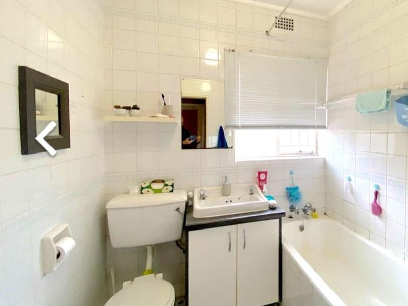 A dated bathroom featuring full-height wall tiling, a built-in vanity with basin, a standard toilet, and a bathtub with shower fixtures.