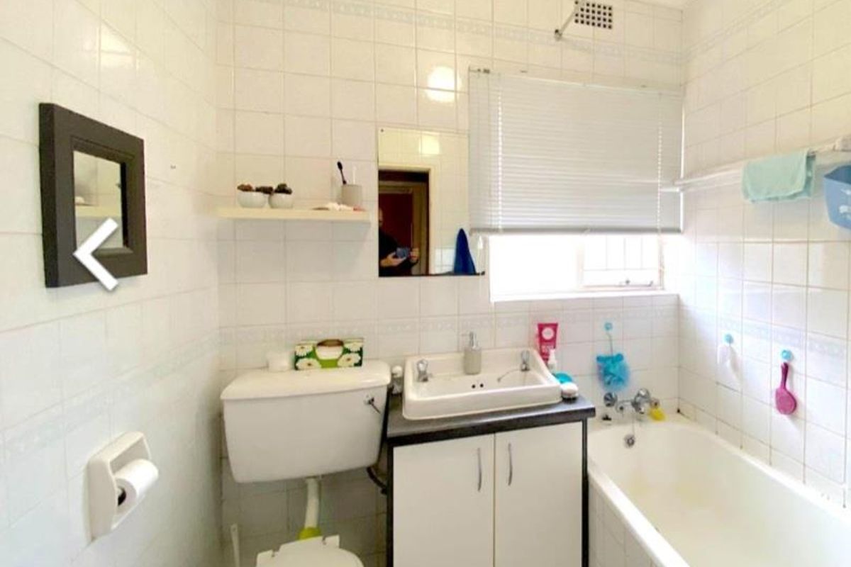 A dated bathroom featuring full-height wall tiling, a built-in vanity with basin, a standard toilet, and a bathtub with shower fixtures.