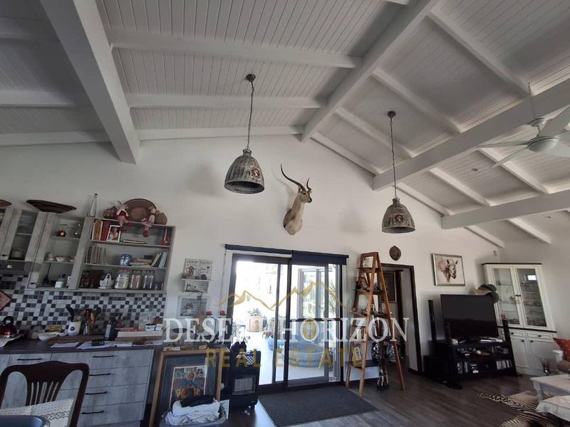 Spacious open-plan living area featuring high exposed beam ceilings, pendant lighting, and direct access to the outdoors through sliding glass doors.