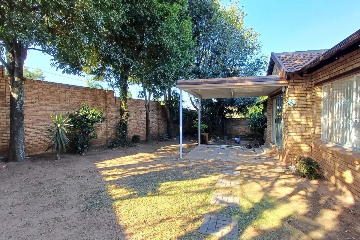Rear exterior view of the townhouse featuring a covered patio, paved walkway, and a private garden enclosed by a brick boundary wall.