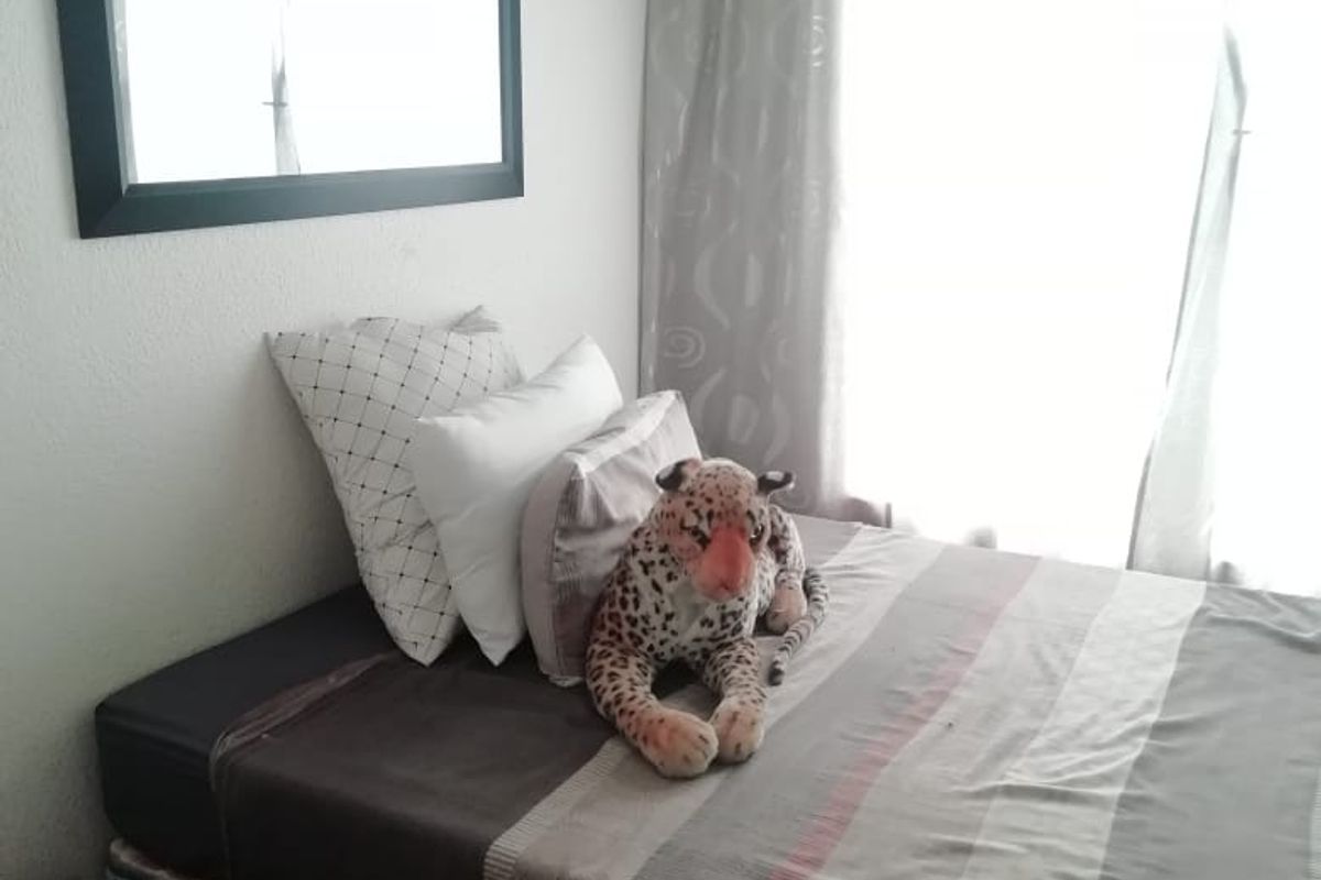 A cozy bedroom featuring a window with curtains and a wall-mounted mirror, providing a functional and comfortable living space.