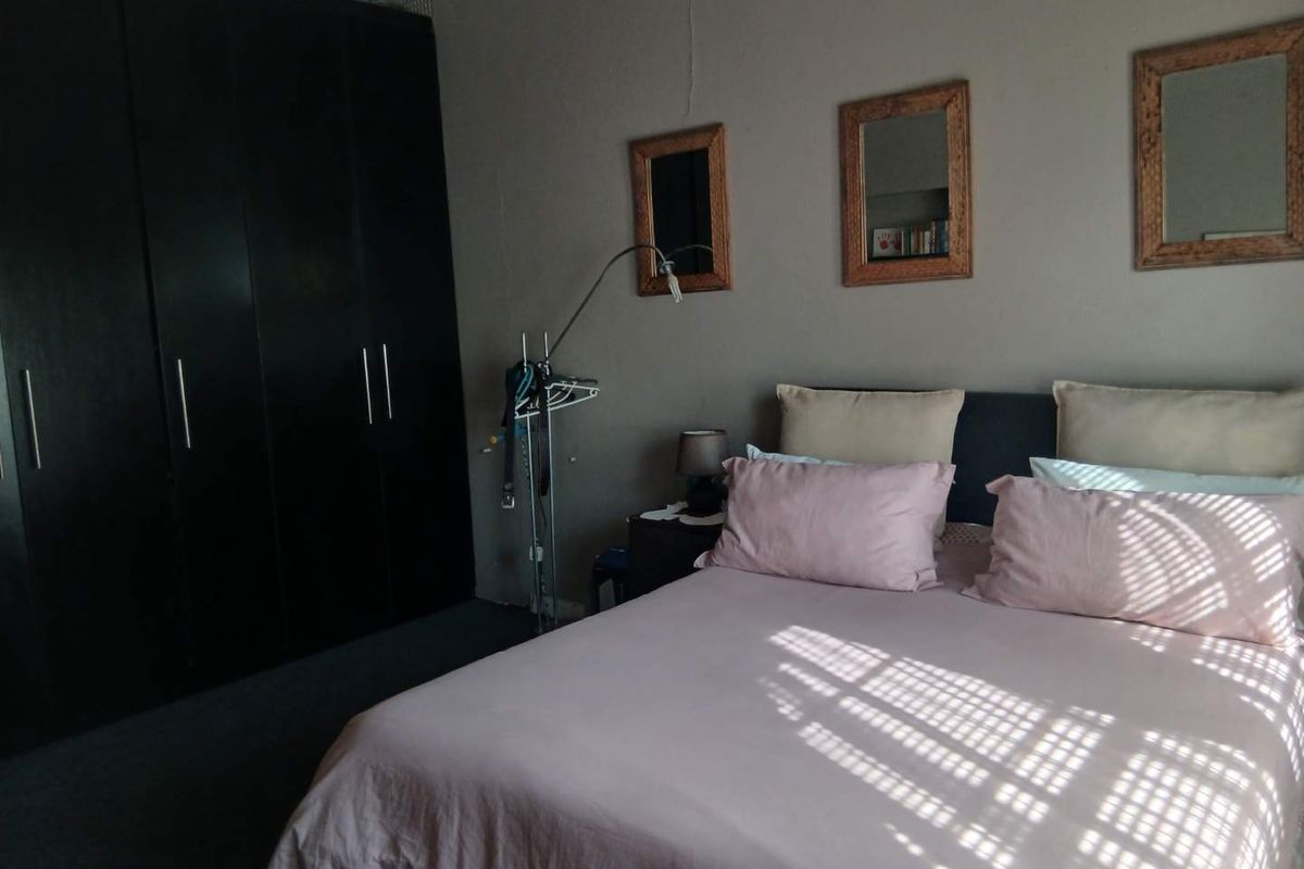 A bedroom featuring a large dark built-in wardrobe and neutral wall finishes, showing signs of minor plaster cracking.