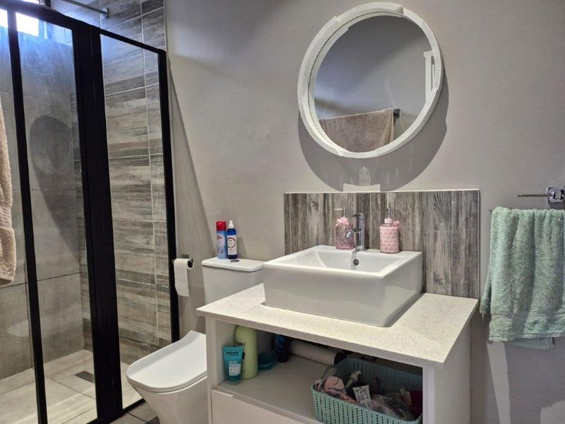 Modern bathroom featuring a vessel sink on a stone vanity, a walk-in shower with a black-framed screen, and contemporary wall tiling.