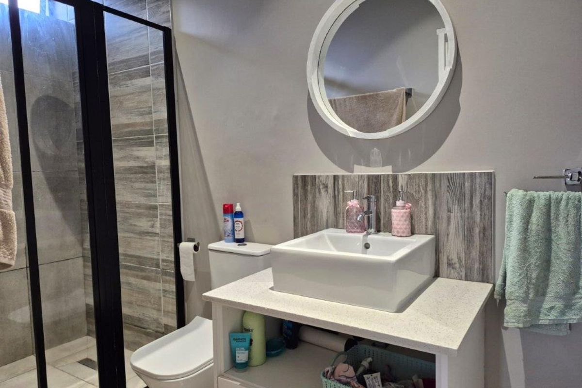 Modern bathroom featuring a vessel sink on a stone vanity, a walk-in shower with a black-framed screen, and contemporary wall tiling.