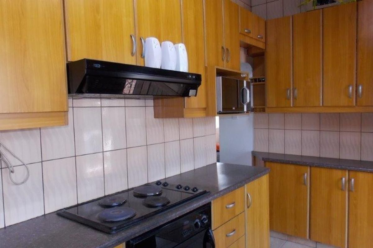 A functional kitchen featuring wood-look laminate cabinetry, dark countertops, a built-in oven, electric hob, and a tiled backsplash.