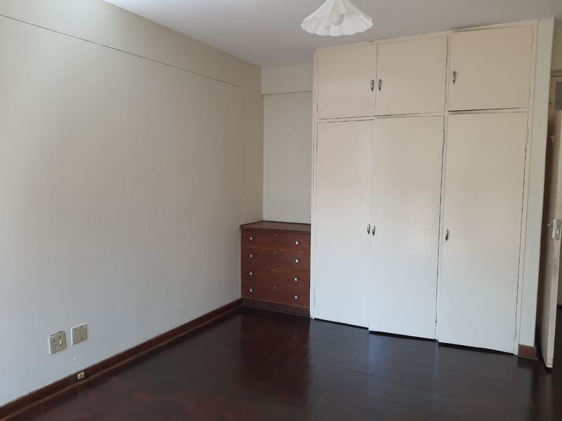 A bedroom featuring dark parquet flooring and extensive built-in storage cupboards, offering a blank canvas for personalization.