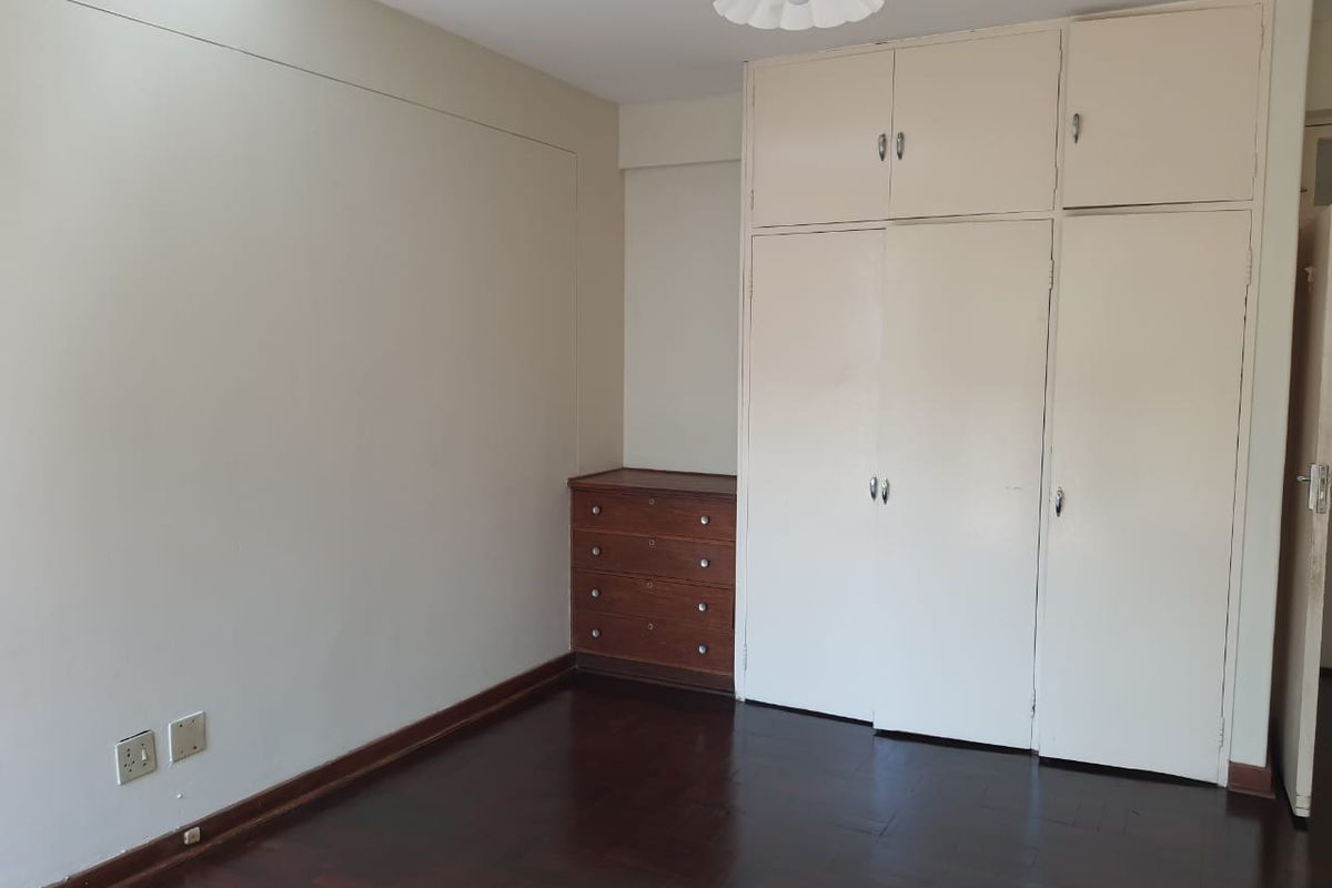 A bedroom featuring dark parquet flooring and extensive built-in storage cupboards, offering a blank canvas for personalization.