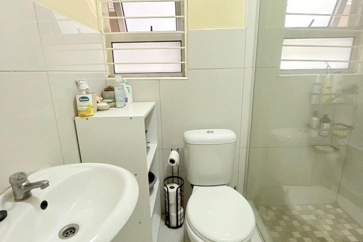 A functional bathroom featuring a pedestal basin, a white toilet, and a glass-enclosed shower with tiled flooring and window ventilation.