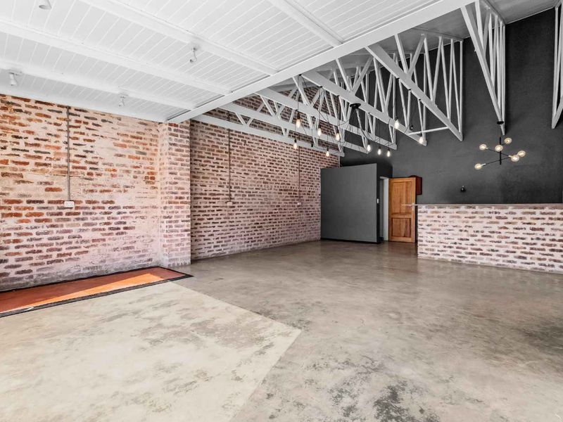 Spacious open-plan living area featuring industrial-style exposed brick walls, polished concrete floors, and high vaulted ceilings with exposed timber trusses.