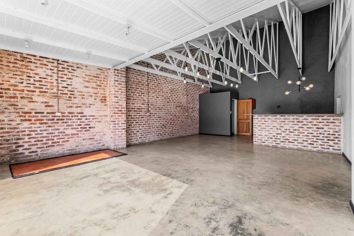 Spacious open-plan living area featuring industrial-style exposed brick walls, polished concrete floors, and high vaulted ceilings with exposed timber trusses.