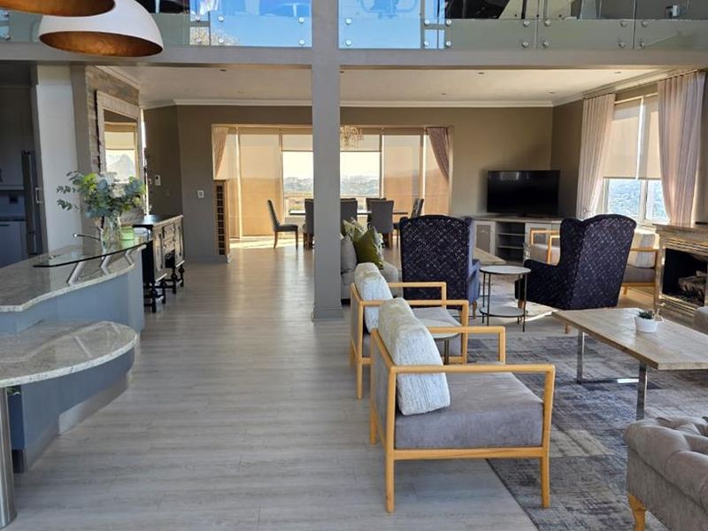 Spacious open-plan living area featuring a modern kitchen island, fireplace, and a mezzanine level with glass balustrades, offering a bright and airy atmosphere.
