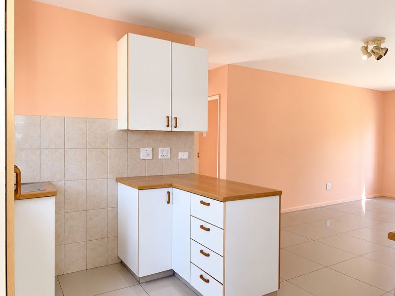 Open plan kitchen area featuring white cabinetry, laminate countertops, and neutral ceramic floor tiles in a well-lit, vacant space.
