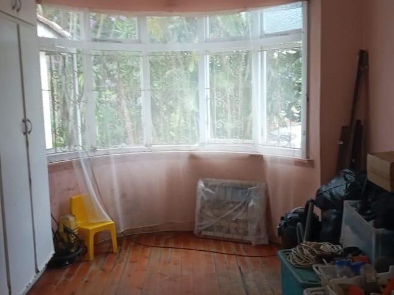 A bedroom featuring built-in cupboards, timber flooring, and a large bay window overlooking the garden.