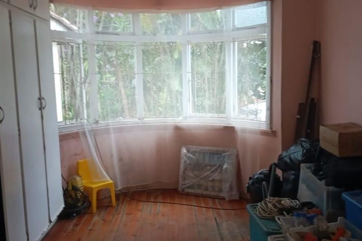 A bedroom featuring built-in cupboards, timber flooring, and a large bay window overlooking the garden.