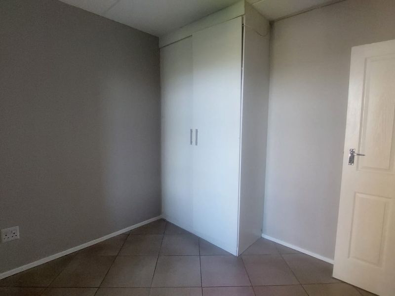 A clean, empty bedroom featuring neutral wall tones, tiled flooring, and a built-in wardrobe, offering a versatile space ready for personalization.