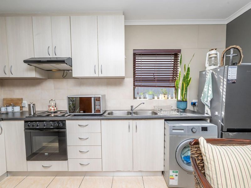 A functional kitchen featuring light-toned cabinetry, dark laminate countertops, a built-in oven with hob, and integrated space for laundry appliances.