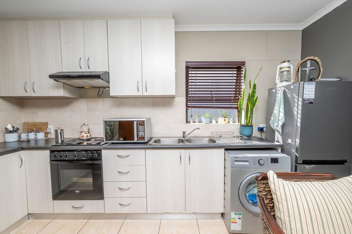 A functional kitchen featuring light-toned cabinetry, dark laminate countertops, a built-in oven with hob, and integrated space for laundry appliances.