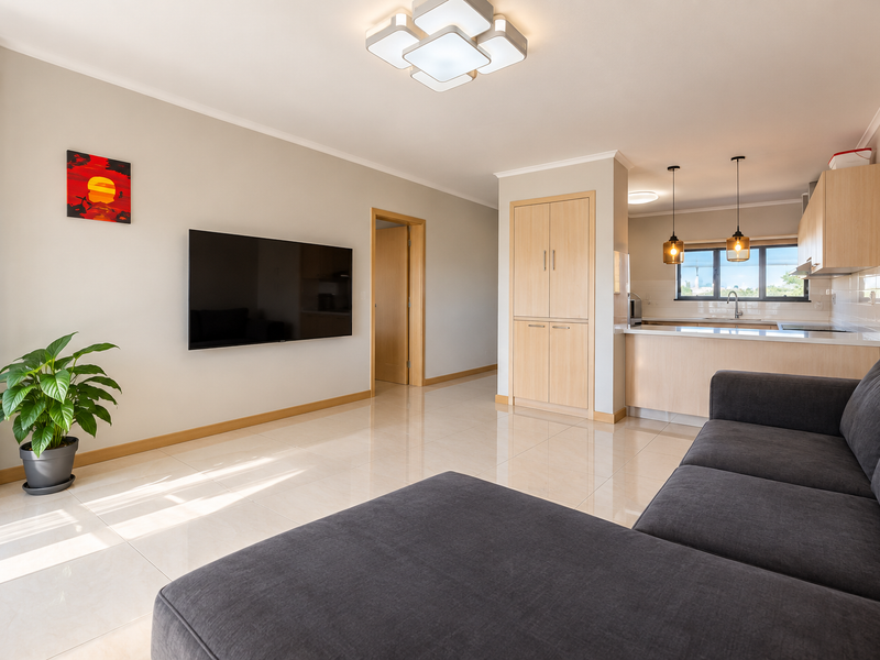 Modern open-plan living area featuring tiled floors, built-in kitchen cabinetry, a functional island, and contemporary lighting fixtures in a well-maintained apartment setting.