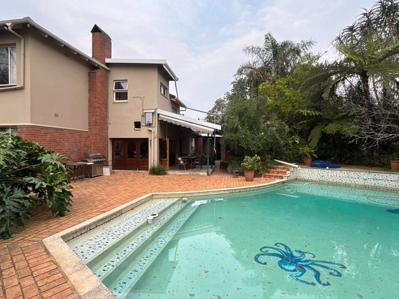 Rear exterior view featuring a swimming pool with tiled steps, a brick patio area, and a retractable awning attached to the house.