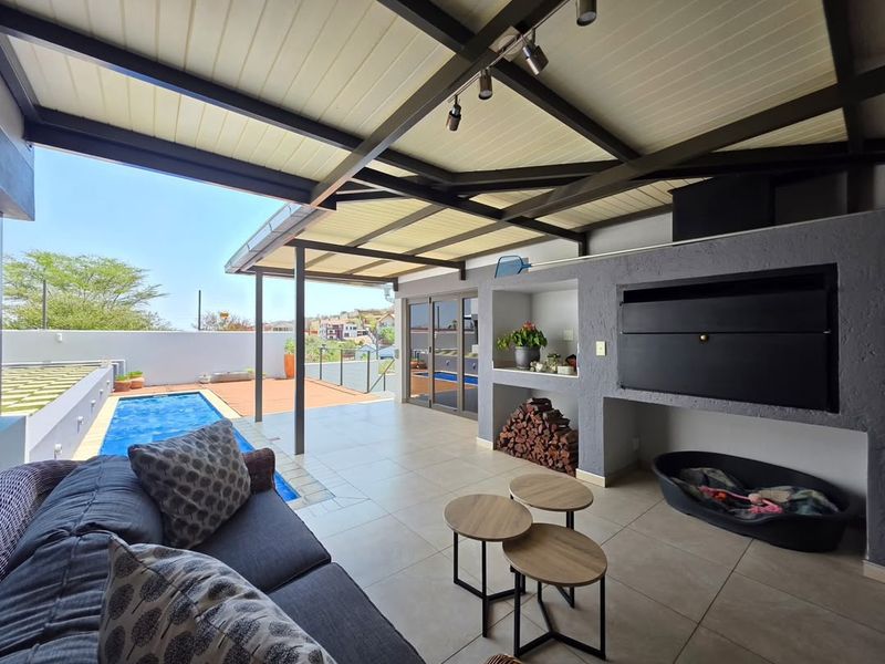 Covered outdoor patio featuring a built-in braai, tiled flooring, and direct access to a swimming pool, perfect for alfresco entertaining.