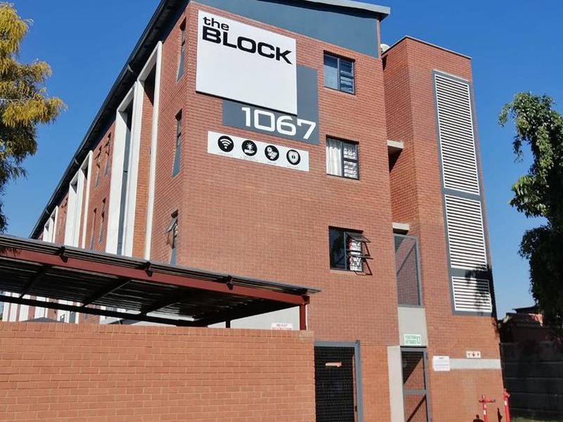 Exterior view of The Block apartment building featuring a modern face brick facade, secure gated entrance, and covered parking area.