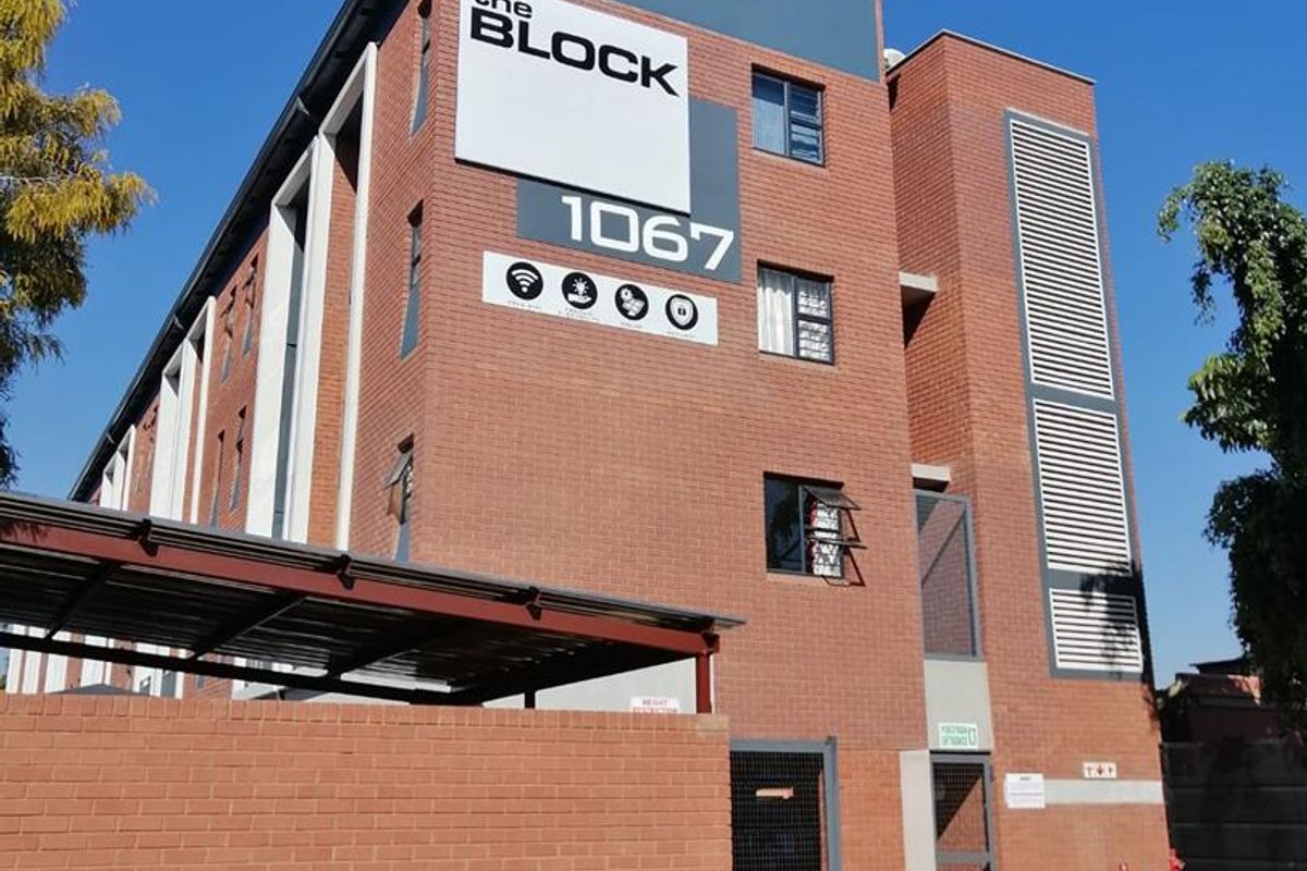 Exterior view of The Block apartment building featuring a modern face brick facade, secure gated entrance, and covered parking area.