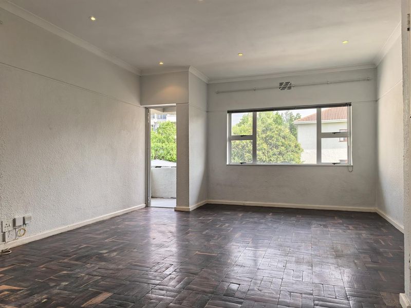 An empty living room featuring dark parquet flooring, recessed lighting, and access to a private balcony through a side door.