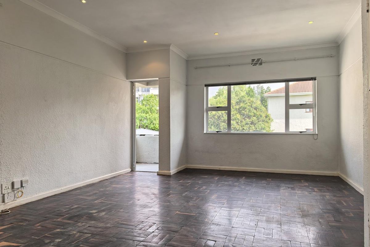 An empty living room featuring dark parquet flooring, recessed lighting, and access to a private balcony through a side door.