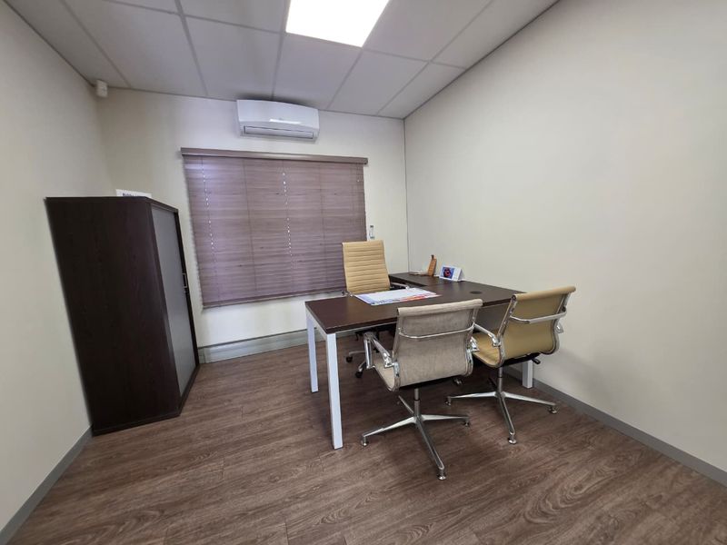 A professional office space featuring laminate flooring, a suspended ceiling, and a wall-mounted split-system air conditioning unit.
