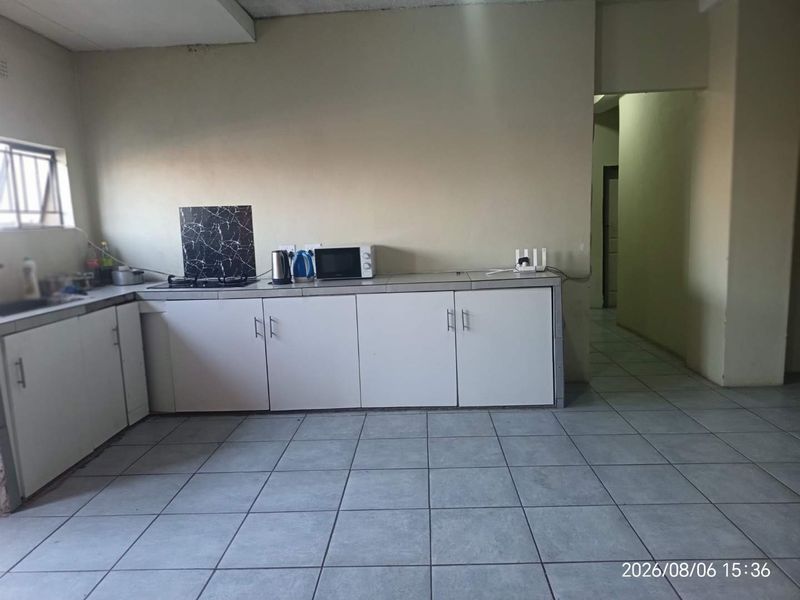 A functional kitchen area featuring tiled flooring, built-in cabinetry, and a hob, offering a blank canvas for potential cosmetic updates and modernization.