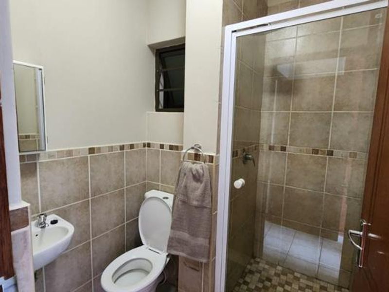 A functional bathroom featuring a shower enclosure, wall-mounted basin, and toilet, finished with neutral wall and floor tiling.