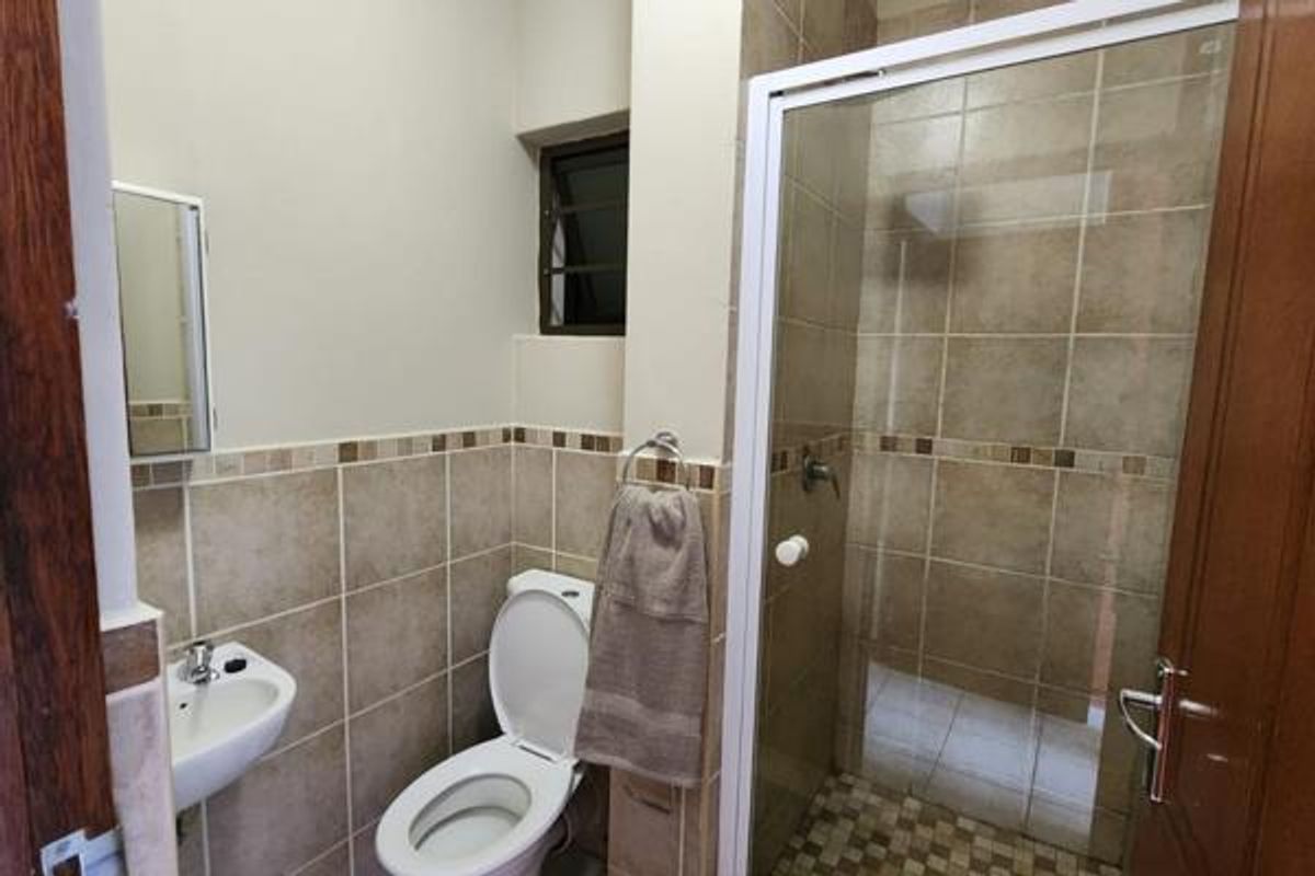 A functional bathroom featuring a shower enclosure, wall-mounted basin, and toilet, finished with neutral wall and floor tiling.