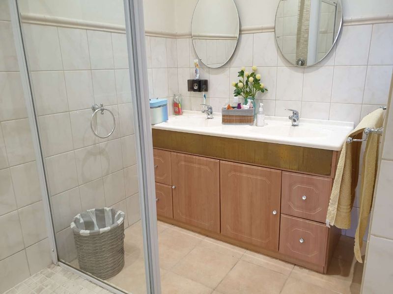 A functional bathroom featuring a double vanity with wood-finish cabinetry, a glass-enclosed shower, and neutral wall and floor tiling.