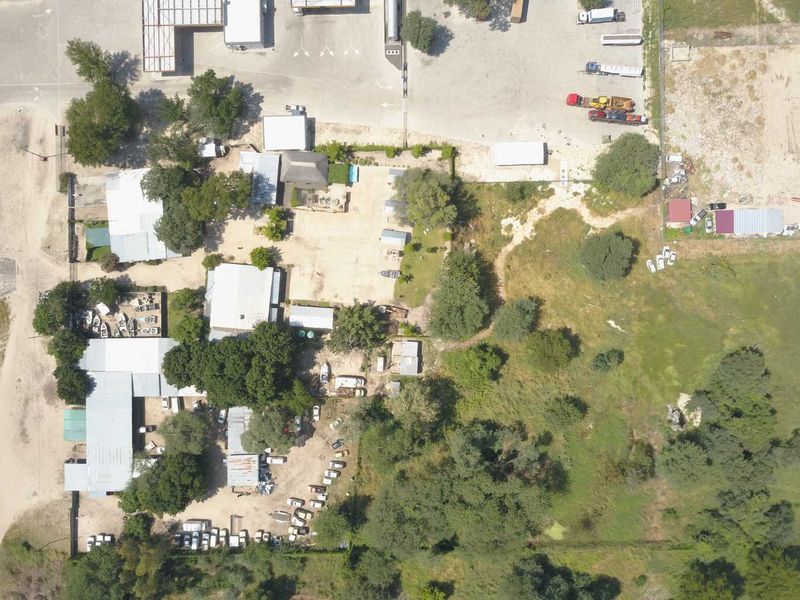Aerial view of a mixed-use property featuring multiple outbuildings, extensive gravel areas, and surrounding natural landscape with mature trees.