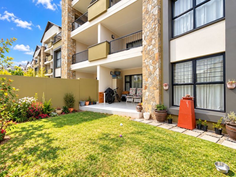 Ground floor apartment featuring a private garden, tiled patio area, and stone-clad exterior facade with modern metal balcony railings.