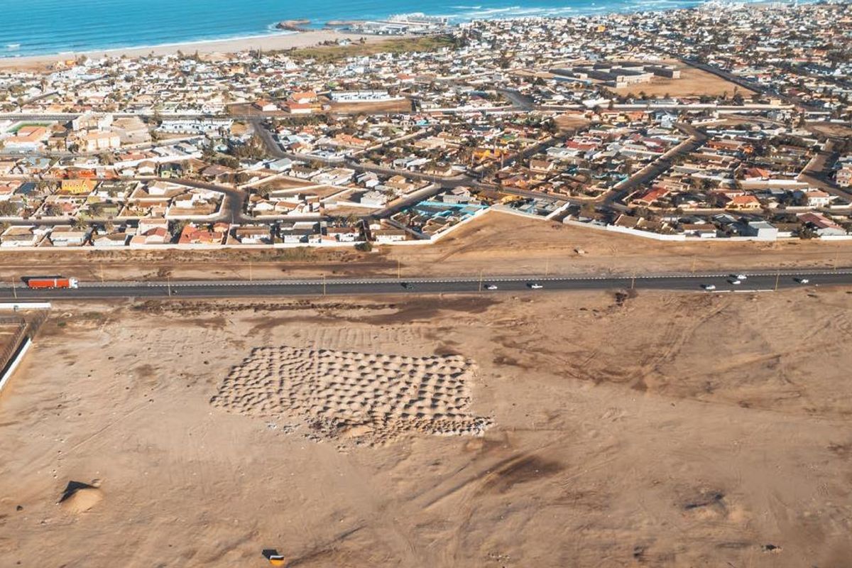 An aerial view showing the surrounding coastal town, main road, and large undeveloped land plot.