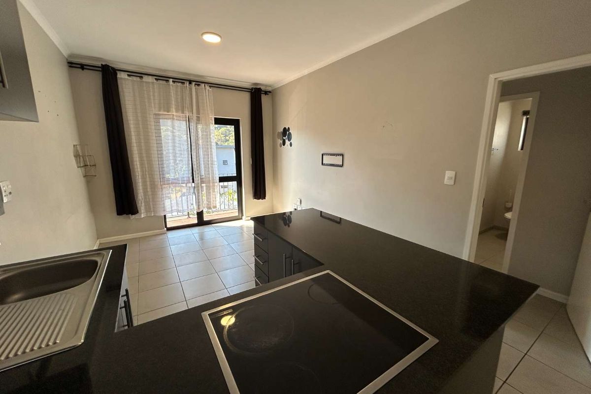 Open-plan kitchen and living area featuring dark granite countertops, electric hob, tiled flooring, and direct access to a balcony through sliding glass doors.