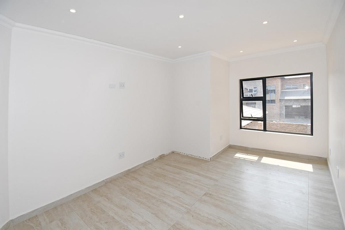 A bright, empty bedroom featuring modern neutral floor tiles, recessed downlighting, and a large window with black aluminium frames.
