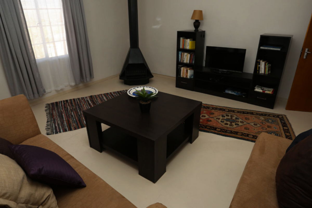 A cozy living room featuring a freestanding black metal fireplace, tiled flooring, and large windows with curtains.