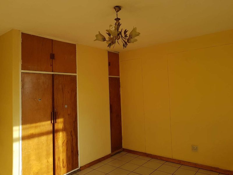 An empty bedroom featuring built-in wooden cupboards, tiled flooring, and a central ceiling light fixture, ready for renovation or restyling.
