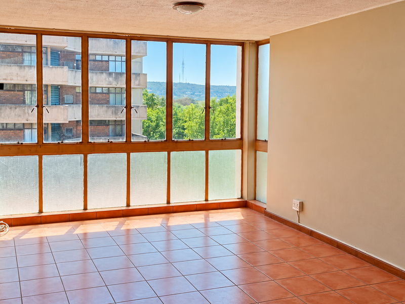 An empty, sunlit living area featuring large multi-pane windows with views, ceramic tiled flooring, and neutral wall finishes, ready for personalization.
