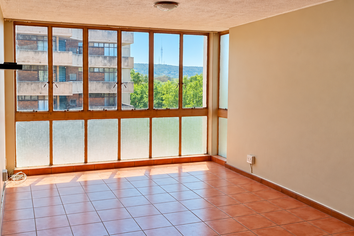 An empty, sunlit living area featuring large multi-pane windows with views, ceramic tiled flooring, and neutral wall finishes, ready for personalization.