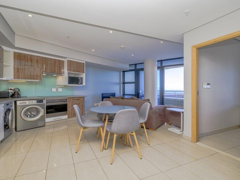 Modern open-plan living area featuring a sleek kitchen with built-in appliances, tiled flooring, and large sliding doors leading to a balcony with ocean views.