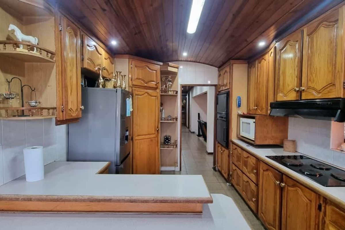 A traditional kitchen featuring extensive wooden cabinetry, laminate countertops, built-in oven, electric hob, and a distinctive timber-paneled ceiling.
