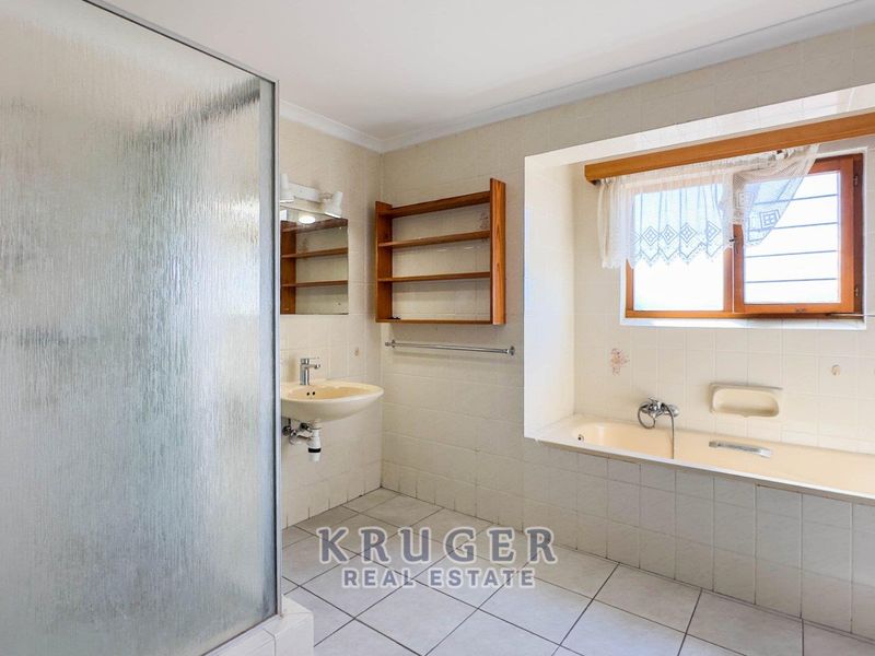 A spacious, dated bathroom featuring a built-in bathtub, separate shower enclosure, and wall-mounted basin with neutral wall and floor tiling.