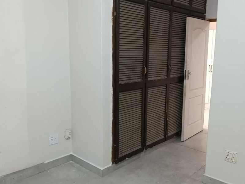A vacant bedroom featuring built-in louvered cupboards and neutral tiled flooring, offering a clean canvas for interior design.