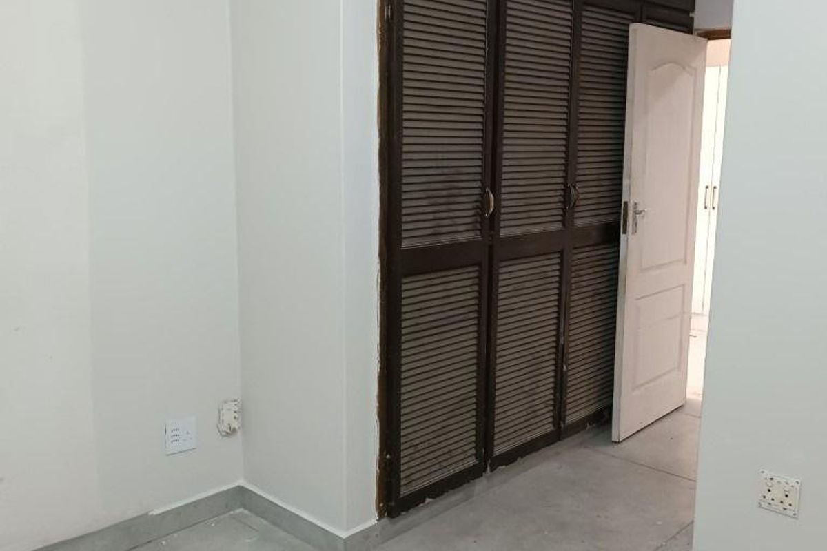 A vacant bedroom featuring built-in louvered cupboards and neutral tiled flooring, offering a clean canvas for interior design.