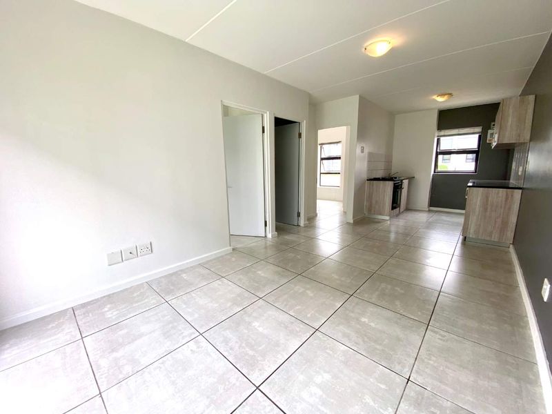 An open-plan living and kitchen area featuring neutral tiled flooring, modern cabinetry, and a built-in stove, offering a clean and versatile living space.