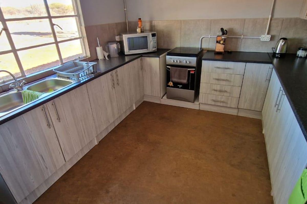 Functional kitchen featuring light wood-grain cabinetry, dark laminate countertops, a stainless steel double sink, and a freestanding stove with a tiled backsplash.
