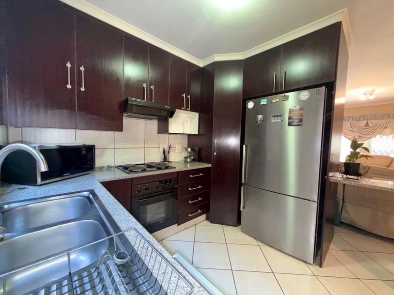 A functional kitchen featuring dark wood cabinetry, granite countertops, a double basin sink, and built-in cooking appliances with tiled flooring and backsplash.